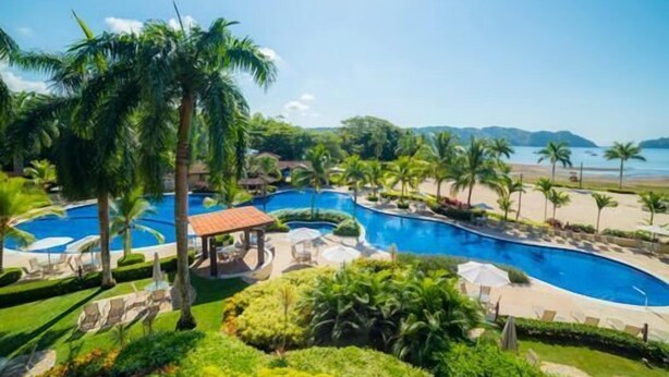 Un resort con varias piscinas, palmeras y vista al mar.