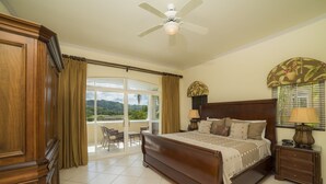 Un dormitorio amplio con una cama grande, un ventilador de techo, una mesita de noche y vistas a un área exterior a través de un ventanal.