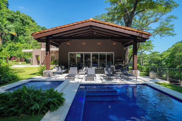 A modern outdoor pool area with a covered seating area and lounge chairs.