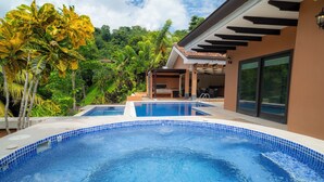 A swimming pool with a tiled edge, surrounded by lush greenery and a modern building with large windows.