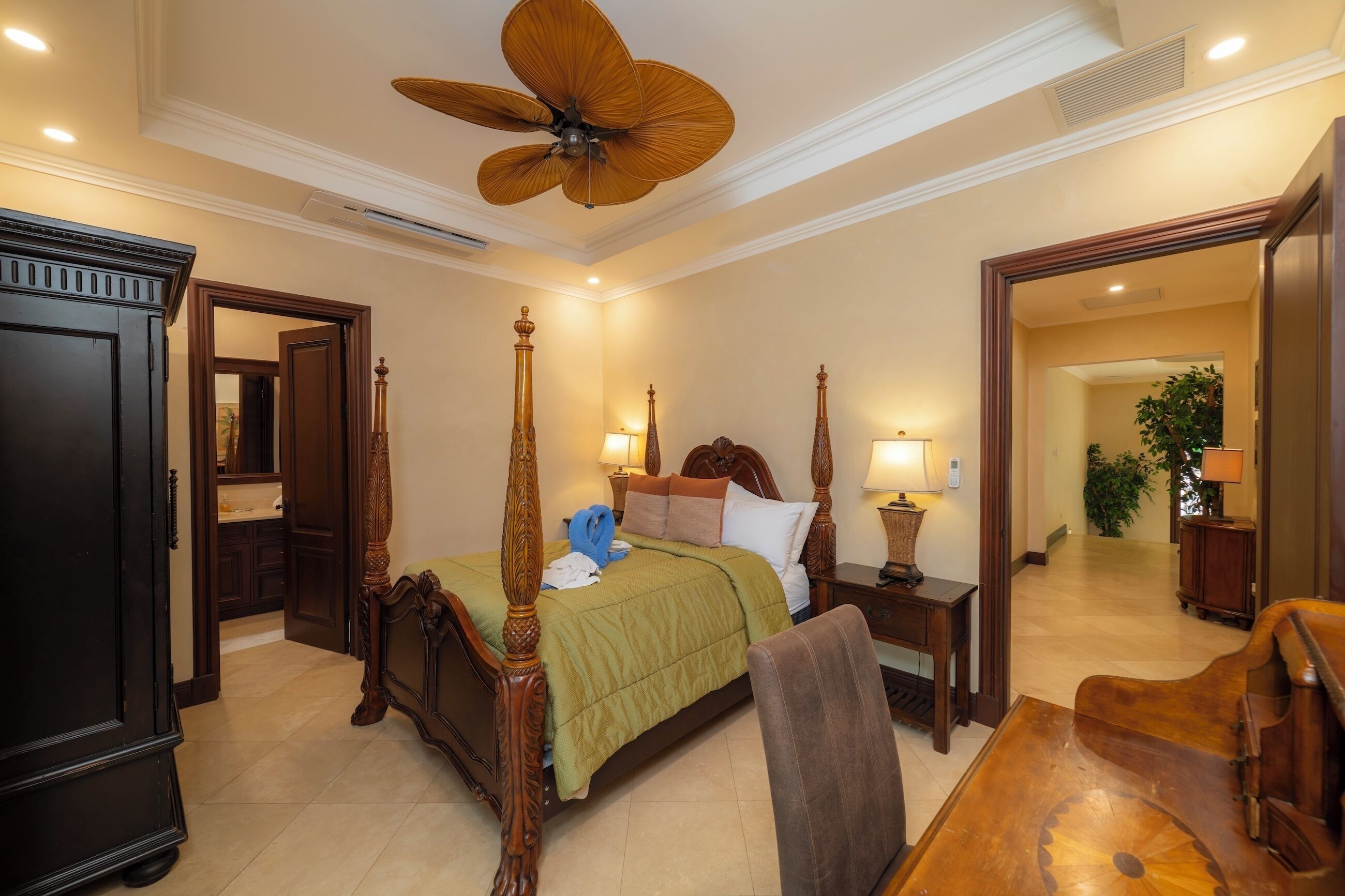 Une chambre d’hôtel avec un lit à baldaquin, un bureau en bois, une chaise, un grand ventilateur de plafond et un miroir.