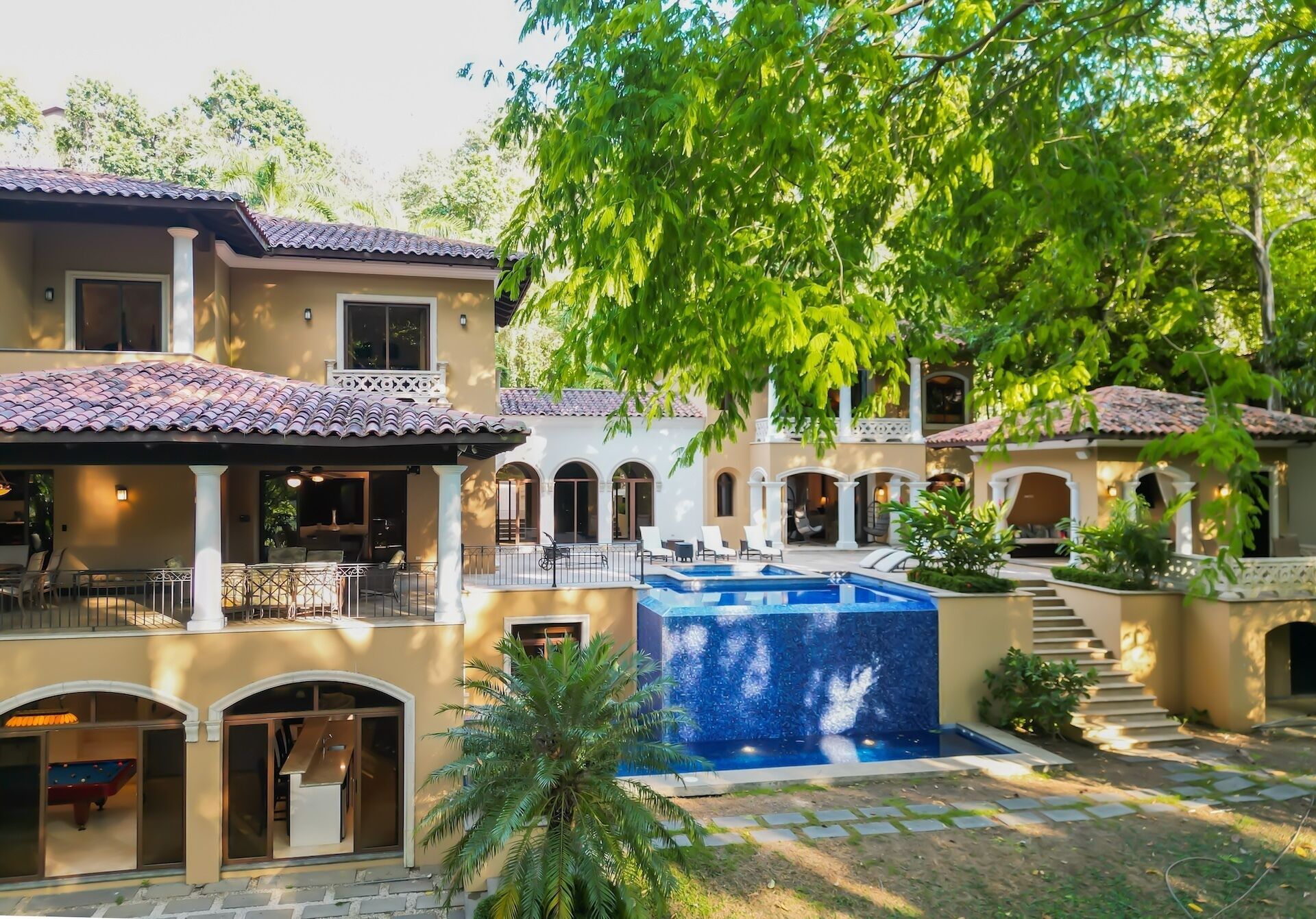 A multi-story house with a swimming pool, outdoor seating, and a covered patio area.