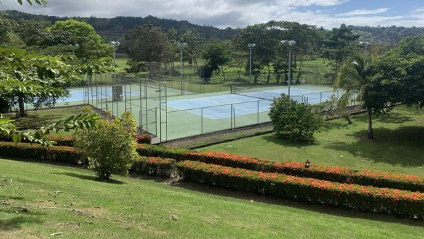 Un court de tennis entouré d’une végétation luxuriante et situé dans un paysage vallonné.