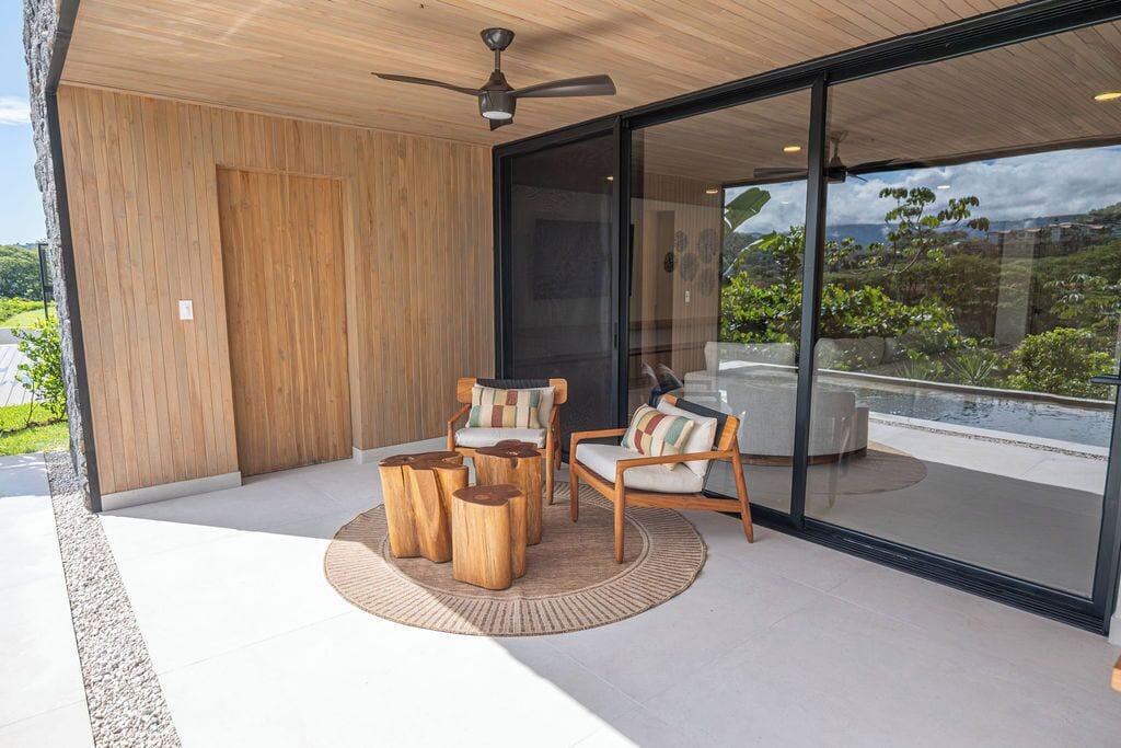 Uma área de estar moderna ao ar livre, com móveis de madeira e uma porta de vidro que dá para uma varanda.