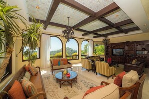 A spacious living room with a high ceiling, large windows, and a cozy seating area. - Los Suenos Luxury Villas by Stay in Costa Rica (Jacó, Costa Rica)