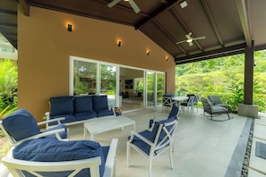 A covered outdoor seating area with a sofa, chairs, and a table, overlooking a lush garden. - Los Suenos Luxury Villas by Stay in Costa Rica (Jacó, Costa Rica)
