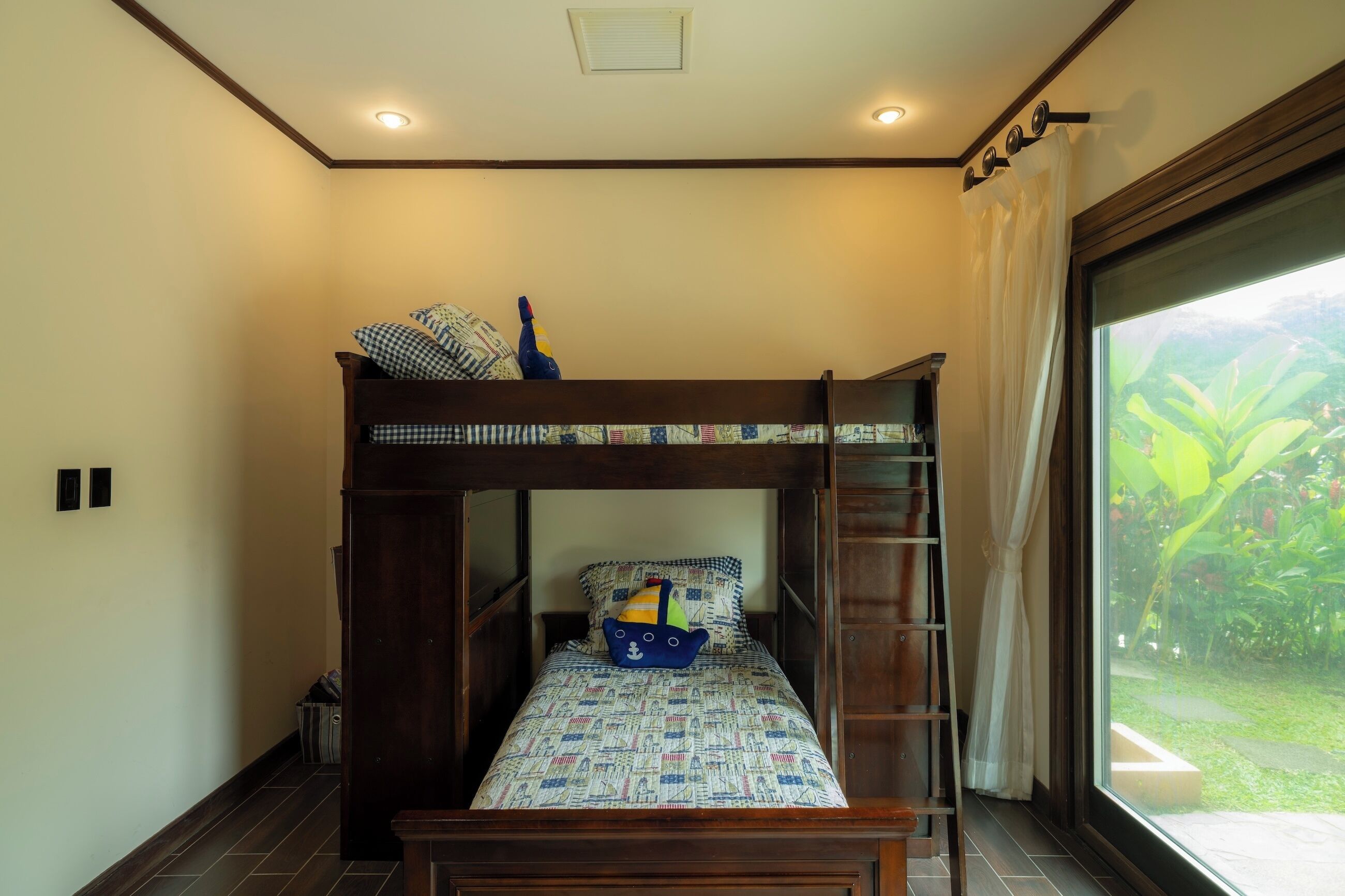 A bunk bed with a patterned bedspread, a small table, and a window with curtains.