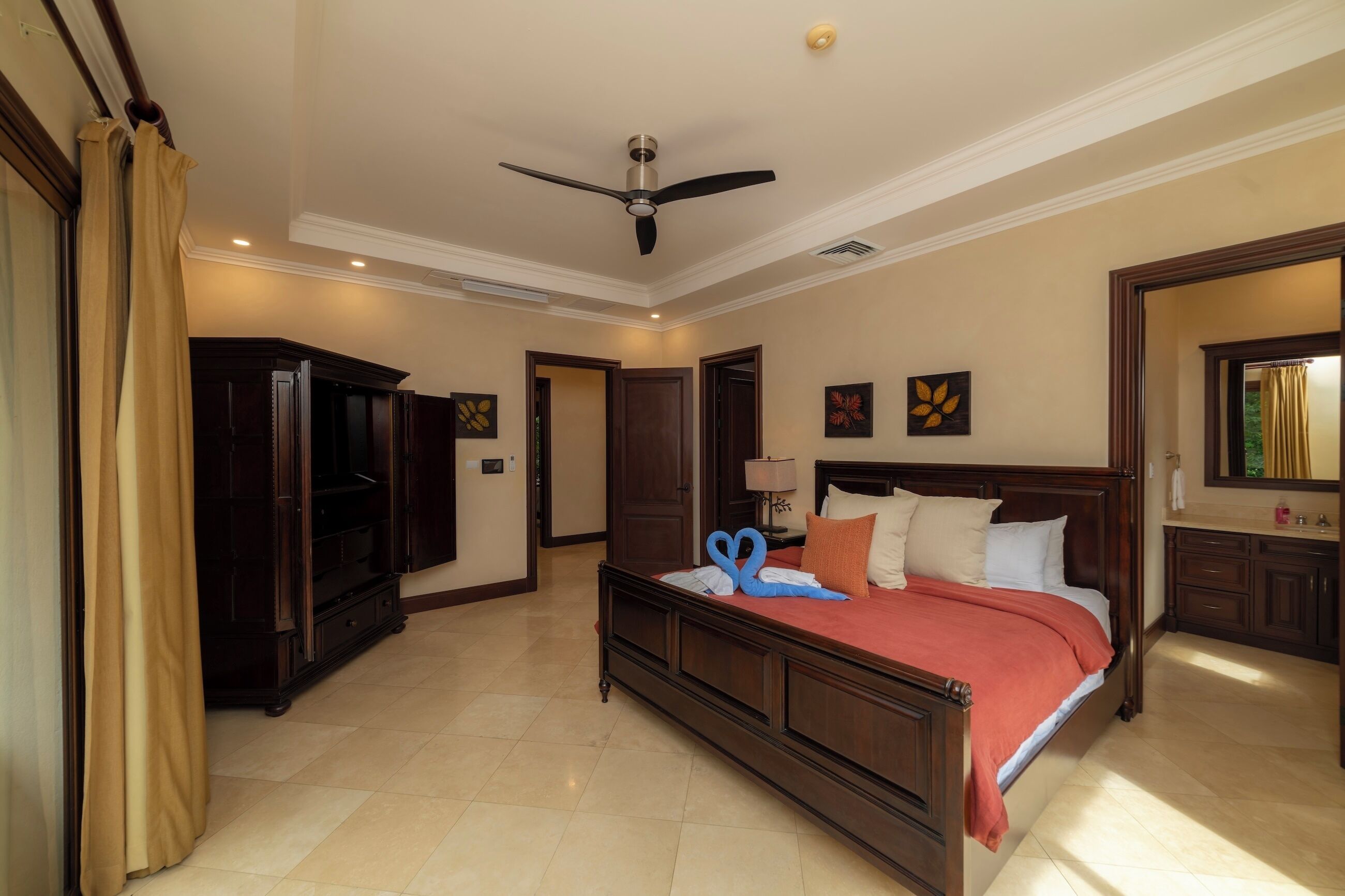 A hotel room with a bed, a ceiling fan, a television, and a bathroom with a mirror.