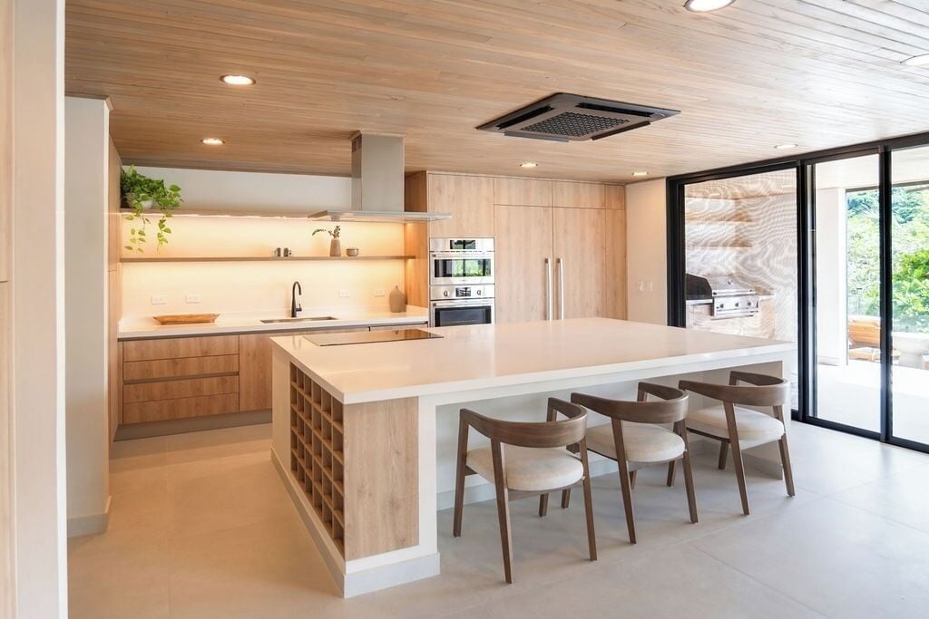 Une cuisine moderne dotée d’un grand îlot central, d’appareils électroménagers intégrés et offrant une vue dégagée grâce à de larges fenêtres.