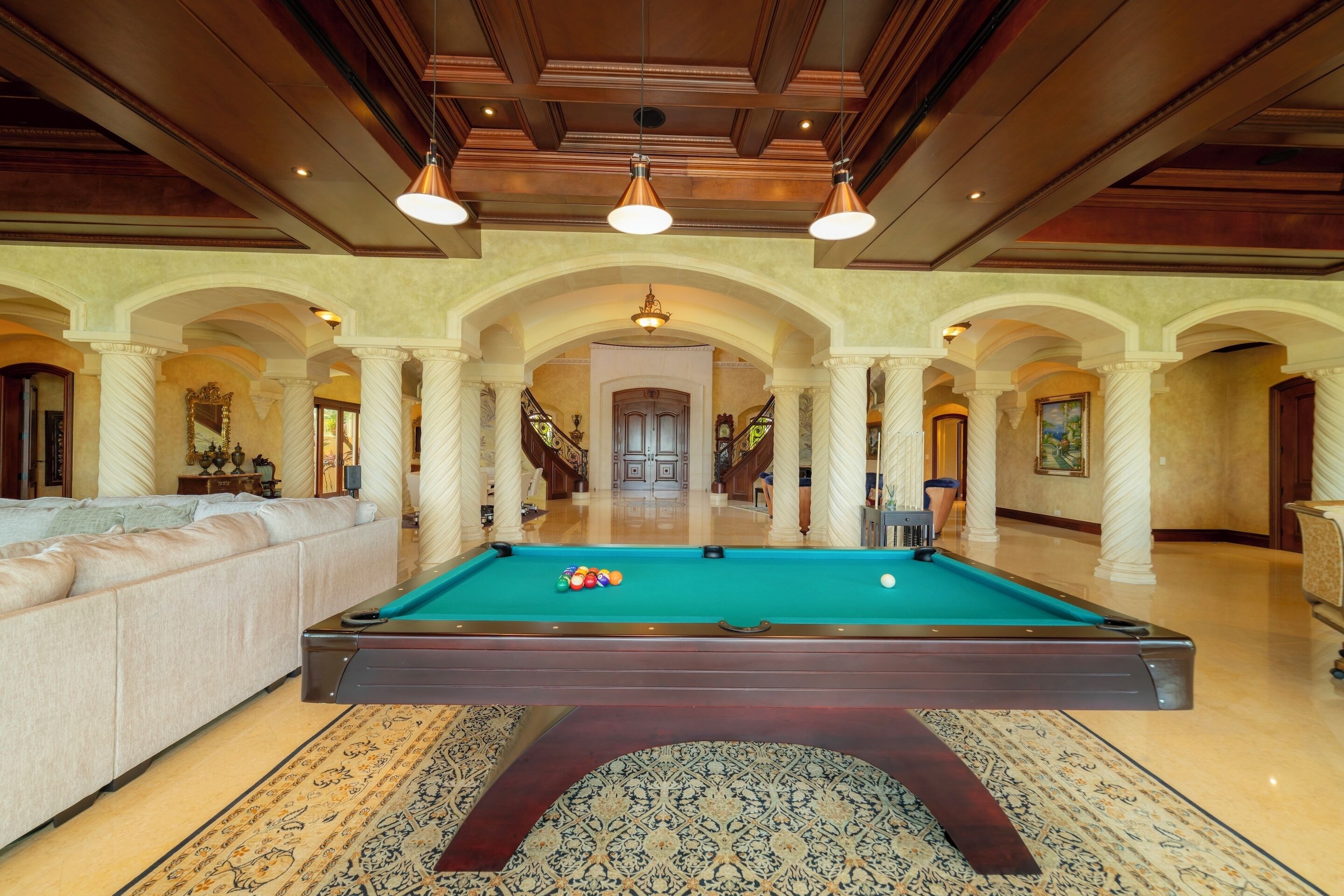 A pool table in a spacious room with a high ceiling and arched columns.