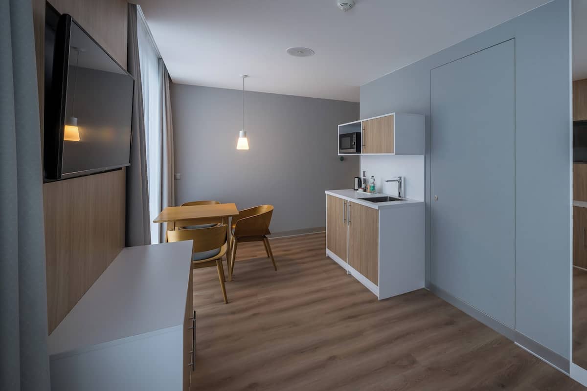 Een moderne keuken met houten kastjes, een wit aanrecht en een eethoek met tafel en stoelen.