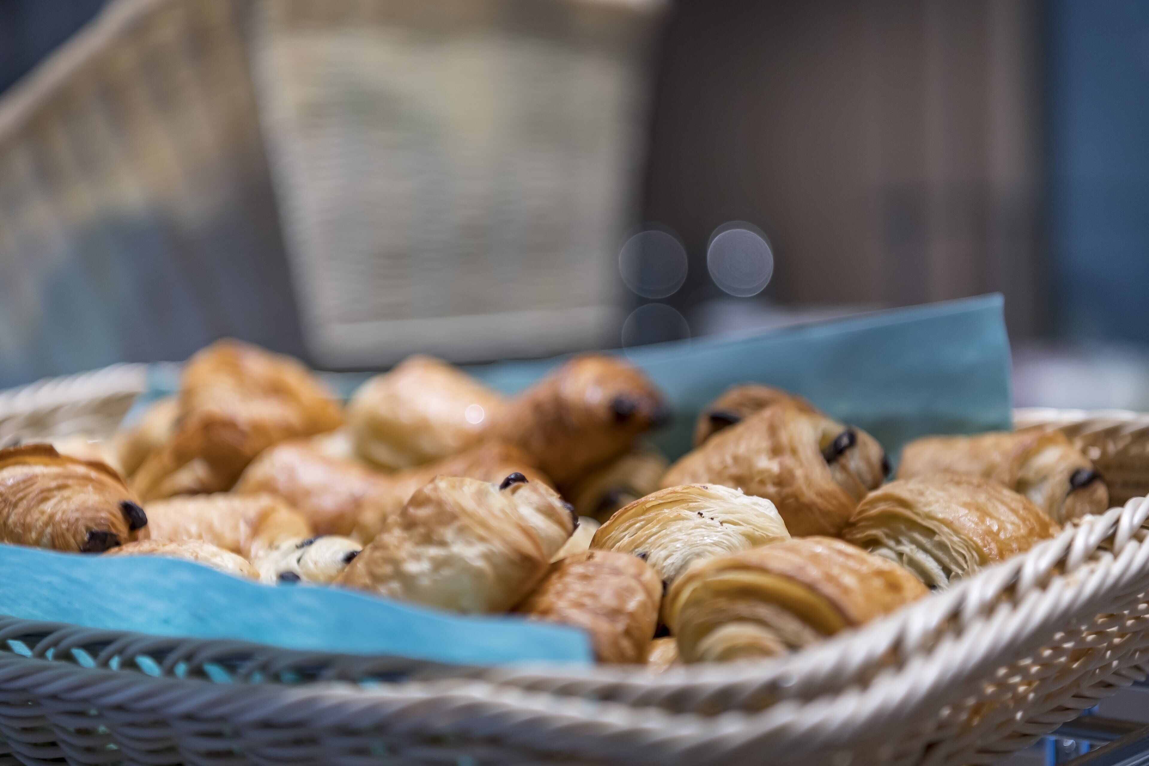 A basket of assorted pastries, including croissants and other baked goods, placed on a blue surface.