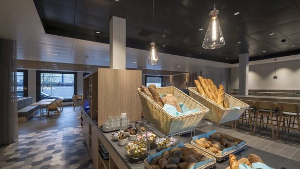 Un buffet de petit-déjeuner moderne avec des paniers en osier remplis de pain, une variété de viennoiseries et un espace repas avec des tables et des chaises.
