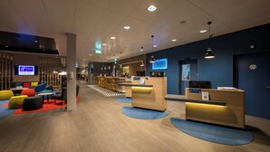Un hall d'hôtel moderne avec un comptoir d'accueil, un espace salon doté de chaises colorées et un bar.