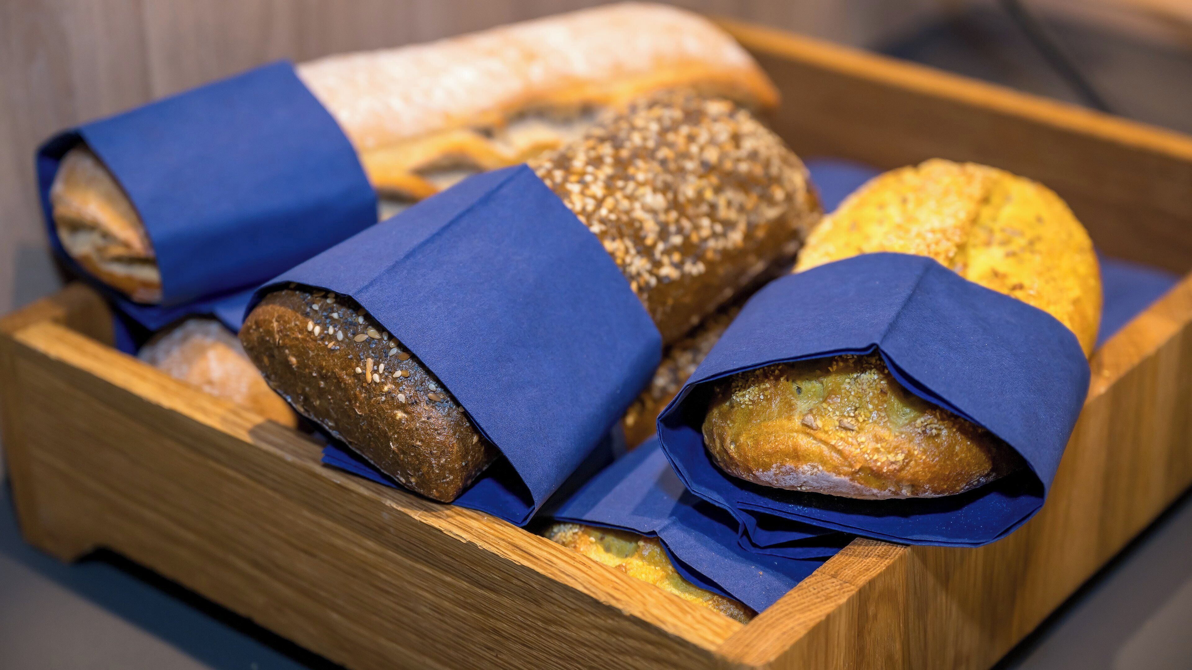 Una bandeja de madera con distintos tipos de pan, algunos envueltos en papel azul.