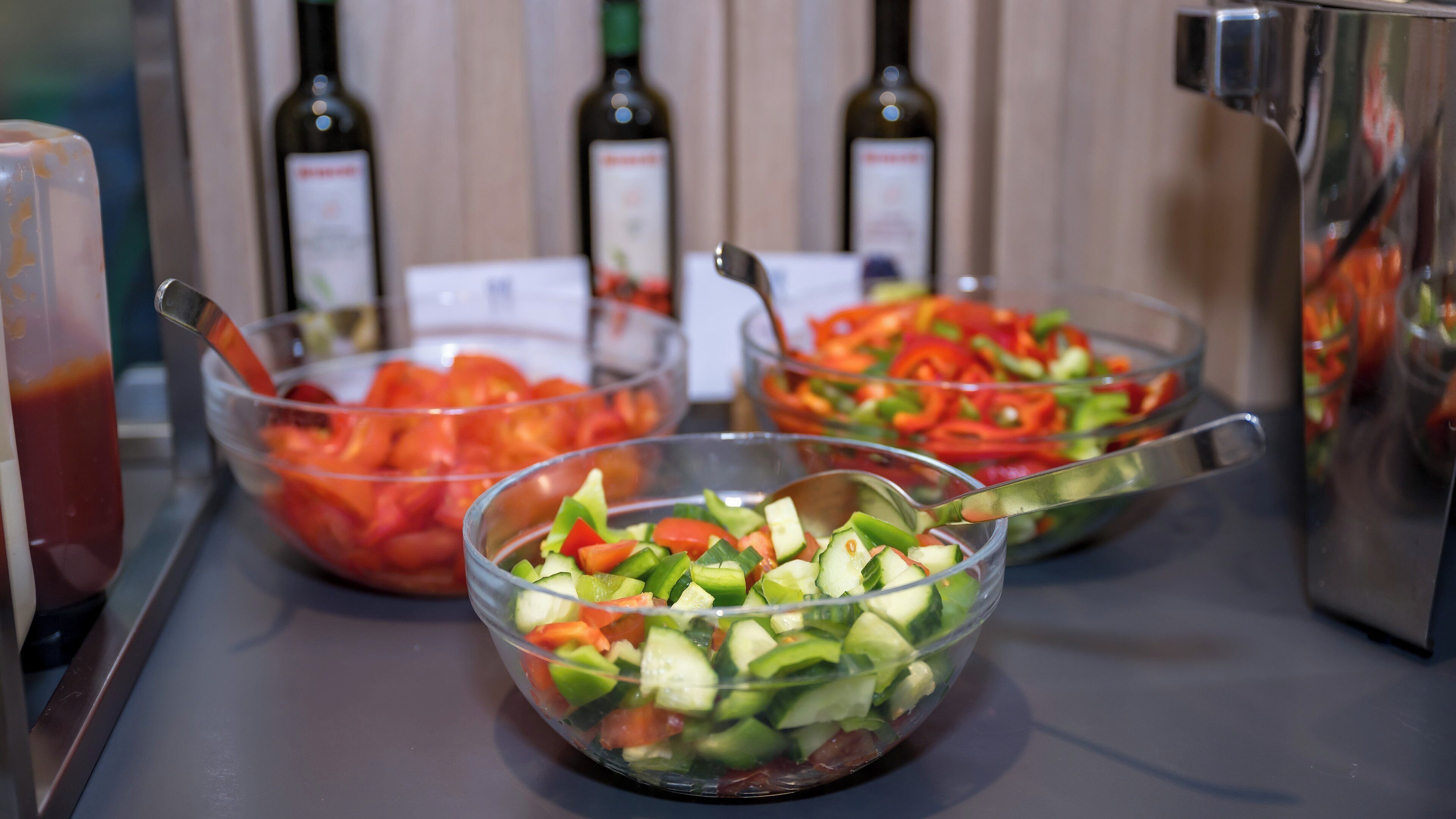 Three bowls of chopped vegetables on a counter with bottles of olive oil in the background.