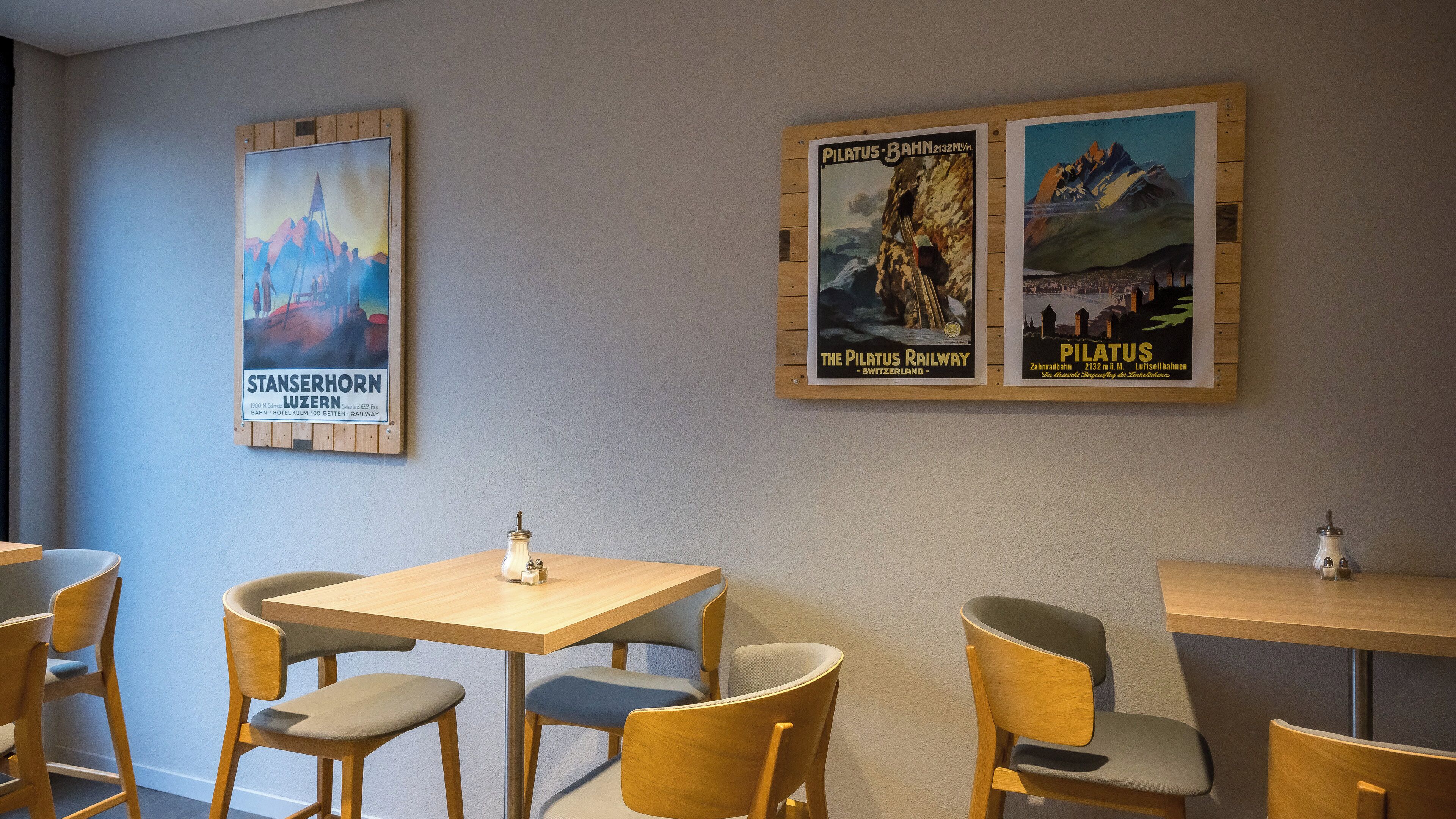 Un comedor con mesas y sillas de madera, una mesita con una botella y salero, y carteles antiguos en la pared.