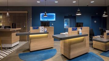 A hotel reception area with multiple counters, a digital screen, and a check-in desk.