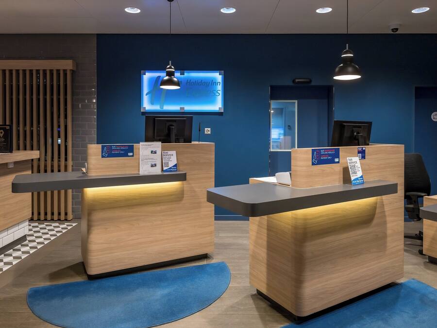 A hotel reception area with multiple counters, a digital screen, and a check-in desk.