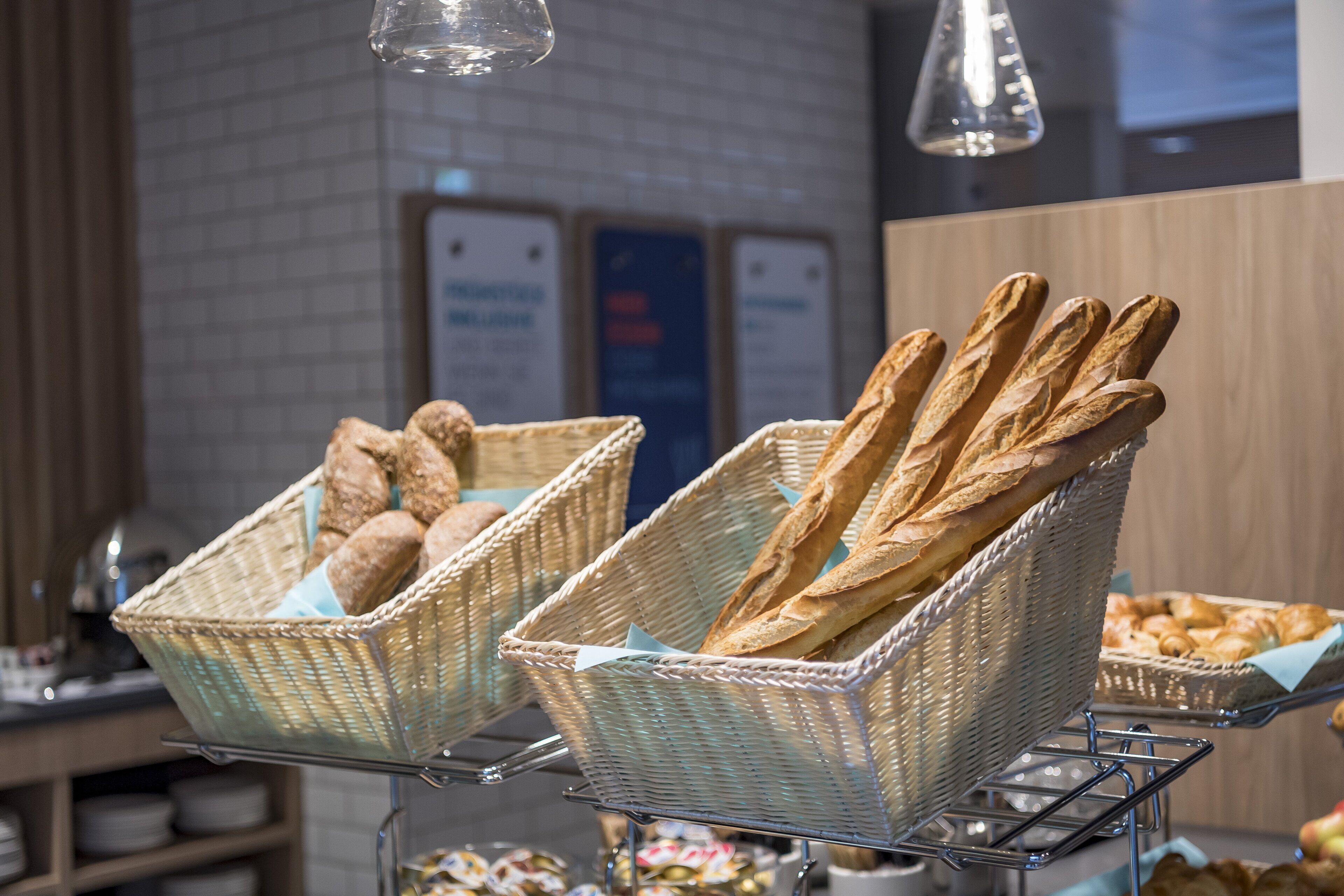 Wicker baskets filled with baguettes and croissants on a metal stand in a bakery.