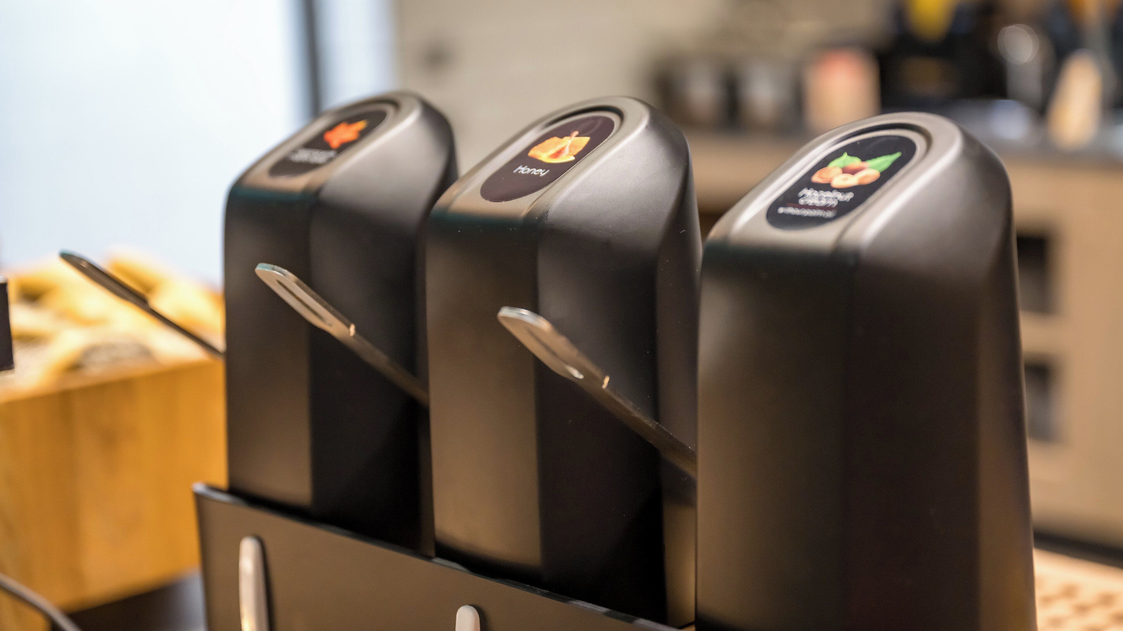 A row of three black, metallic, touch-activated dispensers with different icons, likely for beverages or snacks, mounted on a metal stand.