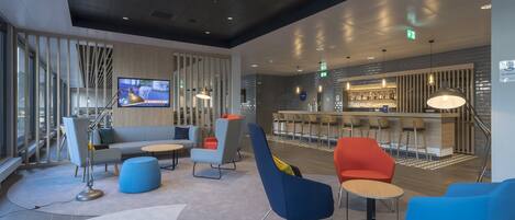 A modern lounge area with seating, a bar, and a television screen.