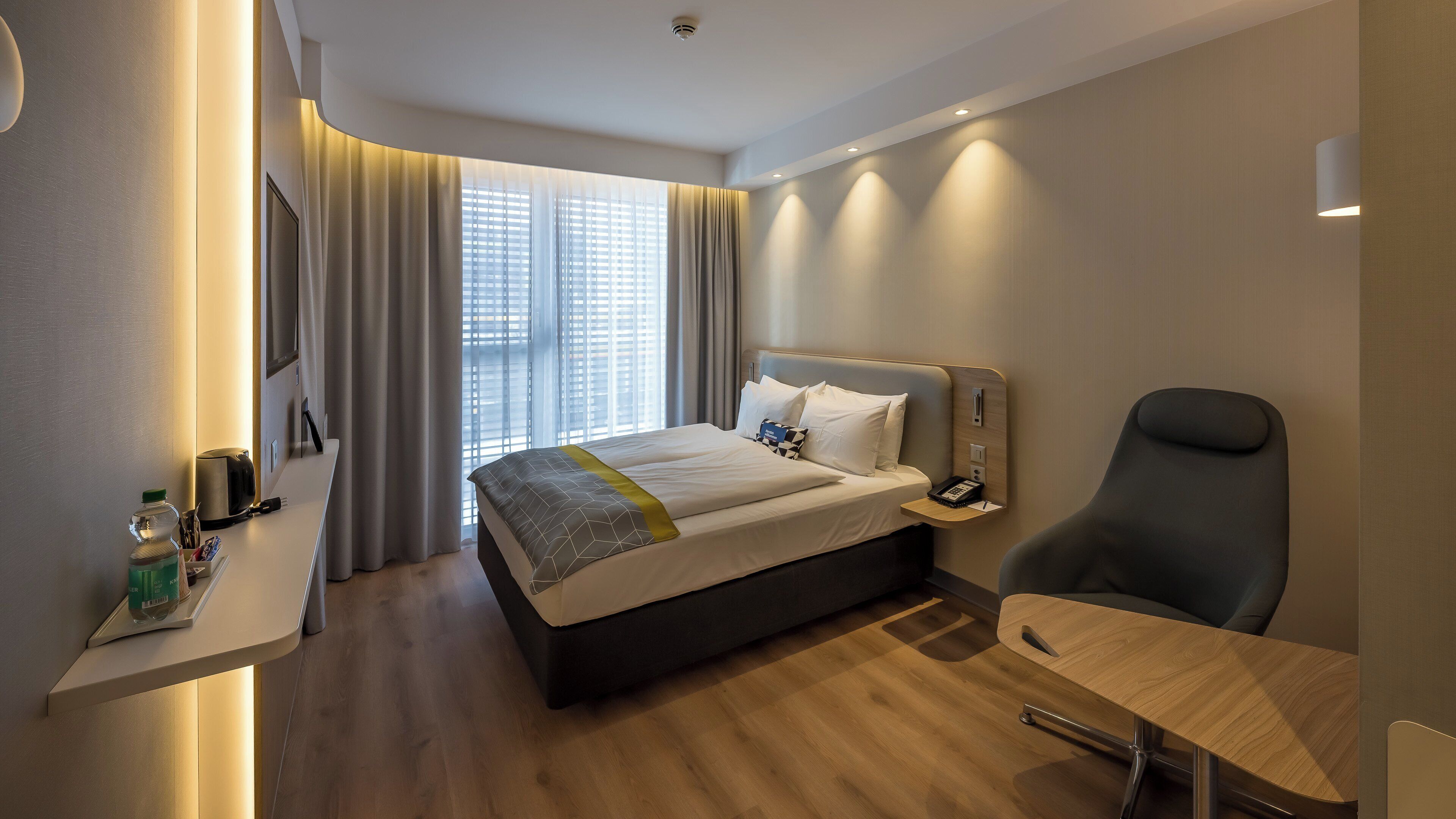 Une chambre d’hôtel comprenant un lit, une table de chevet, une chaise et un bureau avec une lampe.