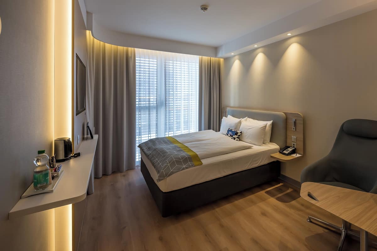 Ein Hotelzimmer mit Bett, Nachttisch, Stuhl und Schreibtisch mit Lampe.