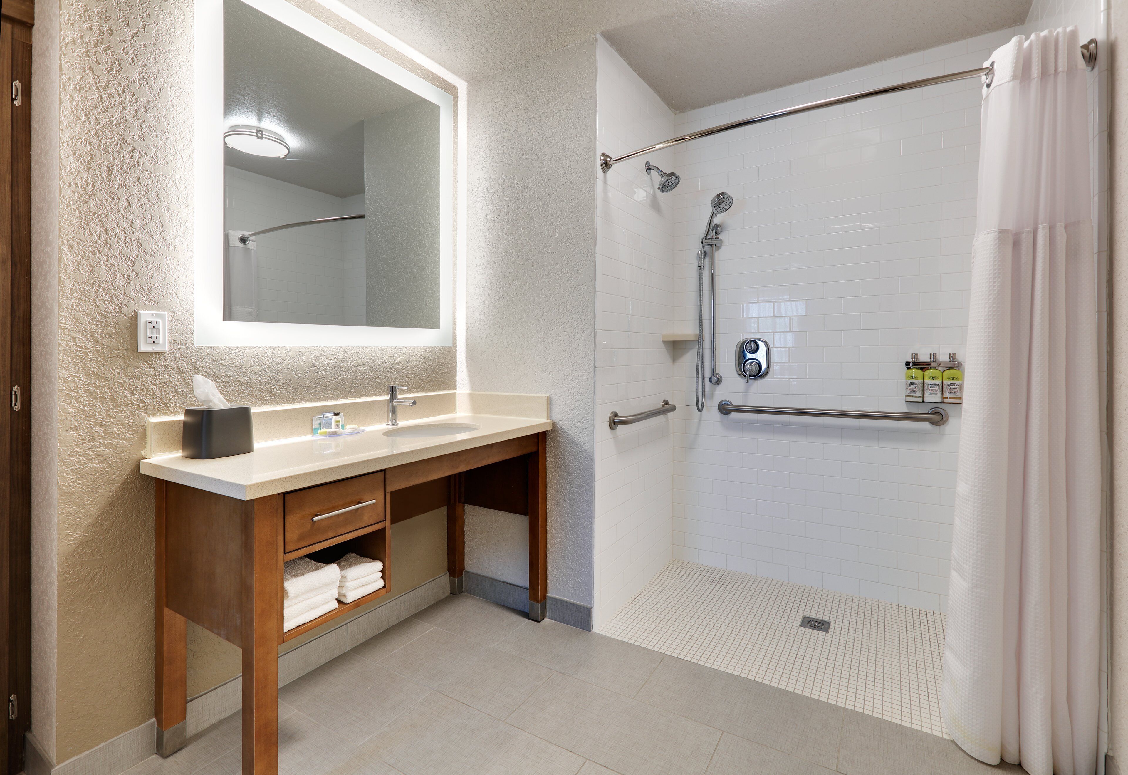 A bathroom with a wooden vanity, a large mirror, a shower with a glass door, and a tiled floor.