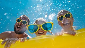 Three people wearing yellow heart-shaped sunglasses, floating on a yellow inflatable raft in a body of water. - Staybridge Suites San Antonio - Schertz  by IHG (Schertz)