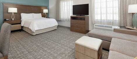 Ein Hotelzimmer mit einem Bett, einem Schreibtisch, einem Fernseher, einer Couch und einem Sessel.