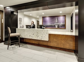 A hotel reception desk with a receptionist, a marble counter, and a framed picture of a bridge. - Staybridge Suites San Antonio - Schertz  by IHG (Schertz)