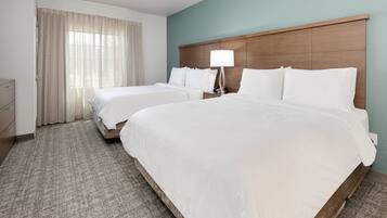 Habitación de hotel con dos camas, una mesita de noche con lámpara, cómoda y ventana con cortinas.