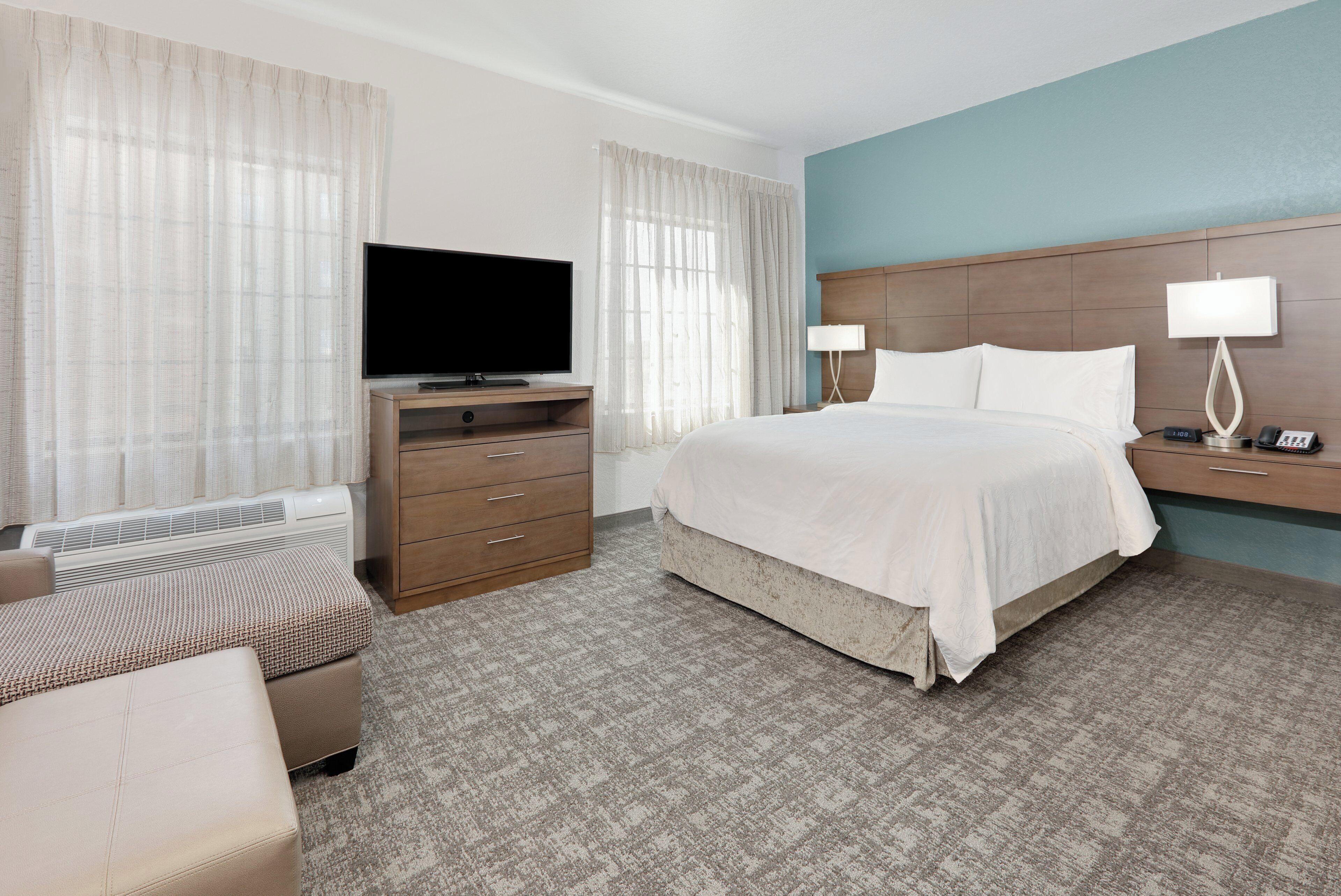 A hotel room with a bed, a television, a desk with a lamp, and a chair.