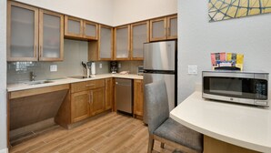 A kitchen with wooden cabinets, a stainless steel refrigerator, a microwave, and a gray chair. - Staybridge Suites San Antonio - Schertz  by IHG (Schertz)