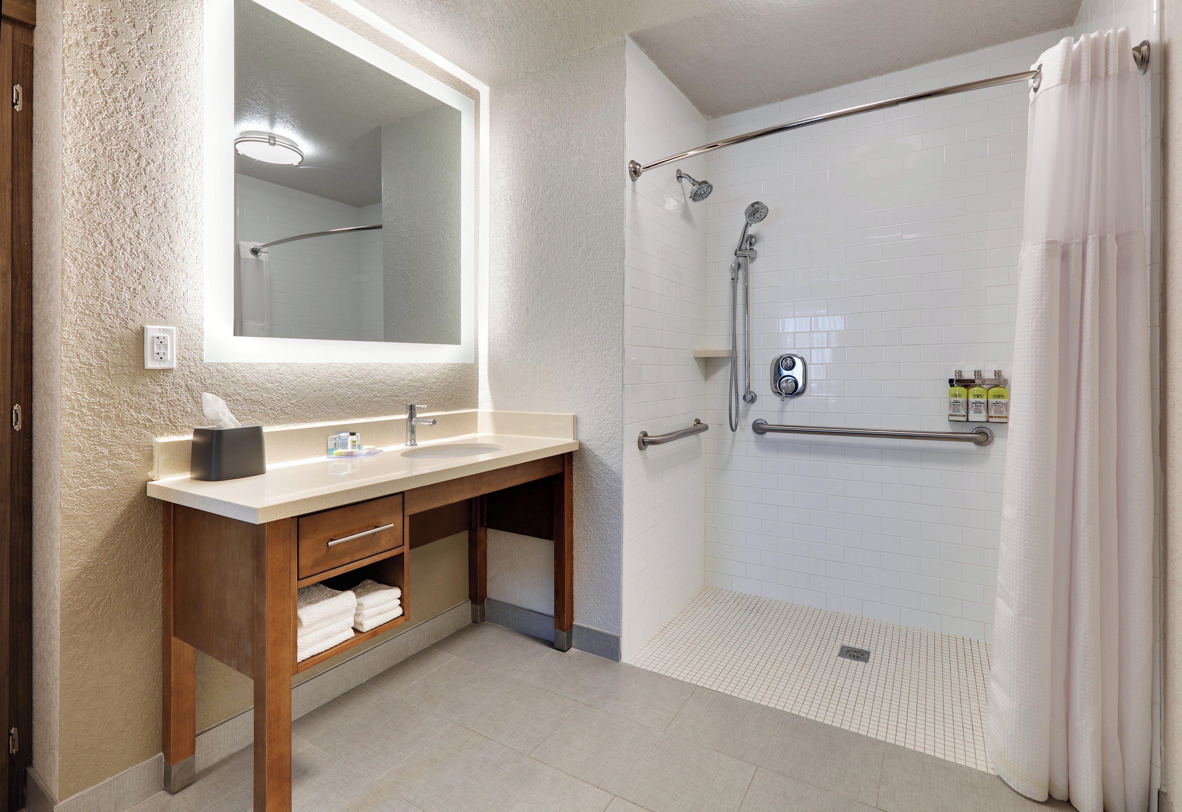 Un baño con tocador de madera, un espejo grande, ducha con puerta de cristal y perchero para toallas.