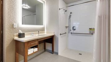 Un baño con tocador de madera, un espejo grande, ducha con puerta de cristal y perchero para toallas.