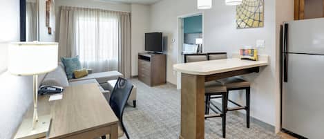 Habitación de hotel pequeña con kitchenette, zona de comedor, espacio de estar con sofá y cama al fondo.