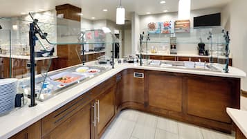 A breakfast buffet area with a glass enclosure, a Coca-Cola machine, and a variety of food items.