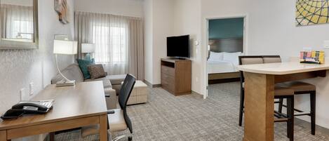 Una habitación de hotel con escritorio, silla, cama, televisor y un cuadro en la pared.