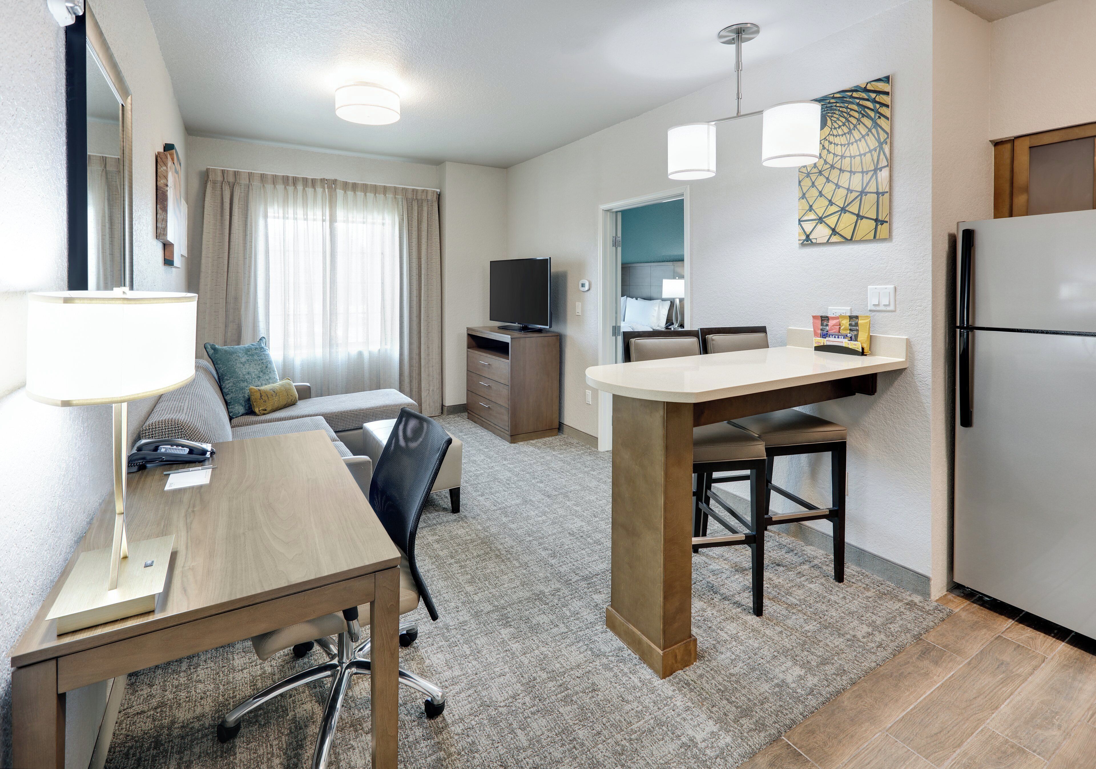 Habitación de hotel compacta con kitchenette, zona de comedor, sofá y televisión.