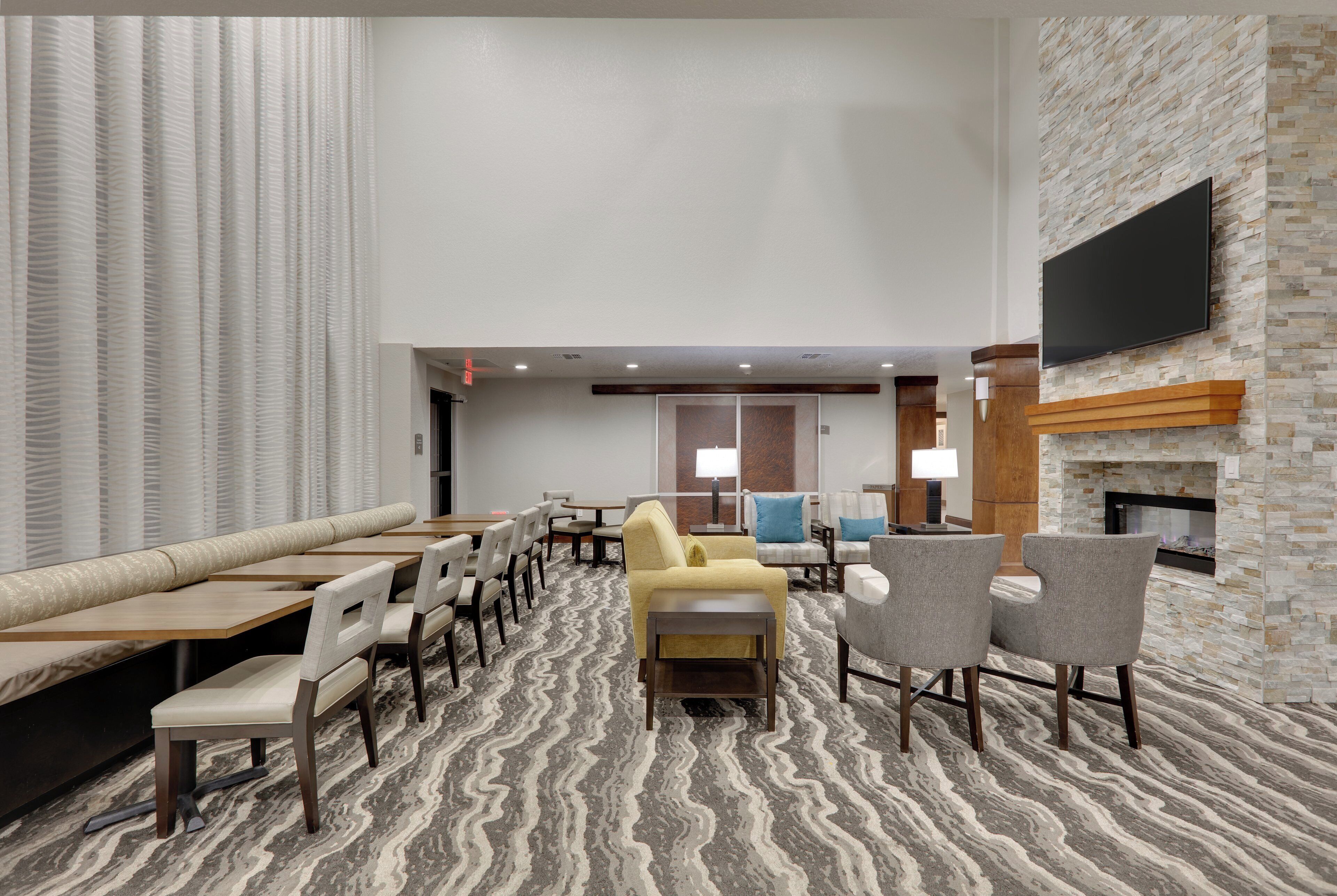 Un hall d’hôtel doté d’un espace salon, d’un téléviseur à écran plat fixé sur un mur en pierre et d’une moquette à motifs.