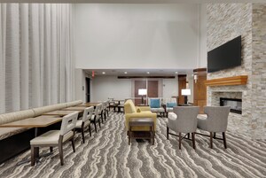 Un vestíbulo de hotel con una zona de estar, un televisor de pantalla plana montado en una pared de piedra y una alfombra estampada.
