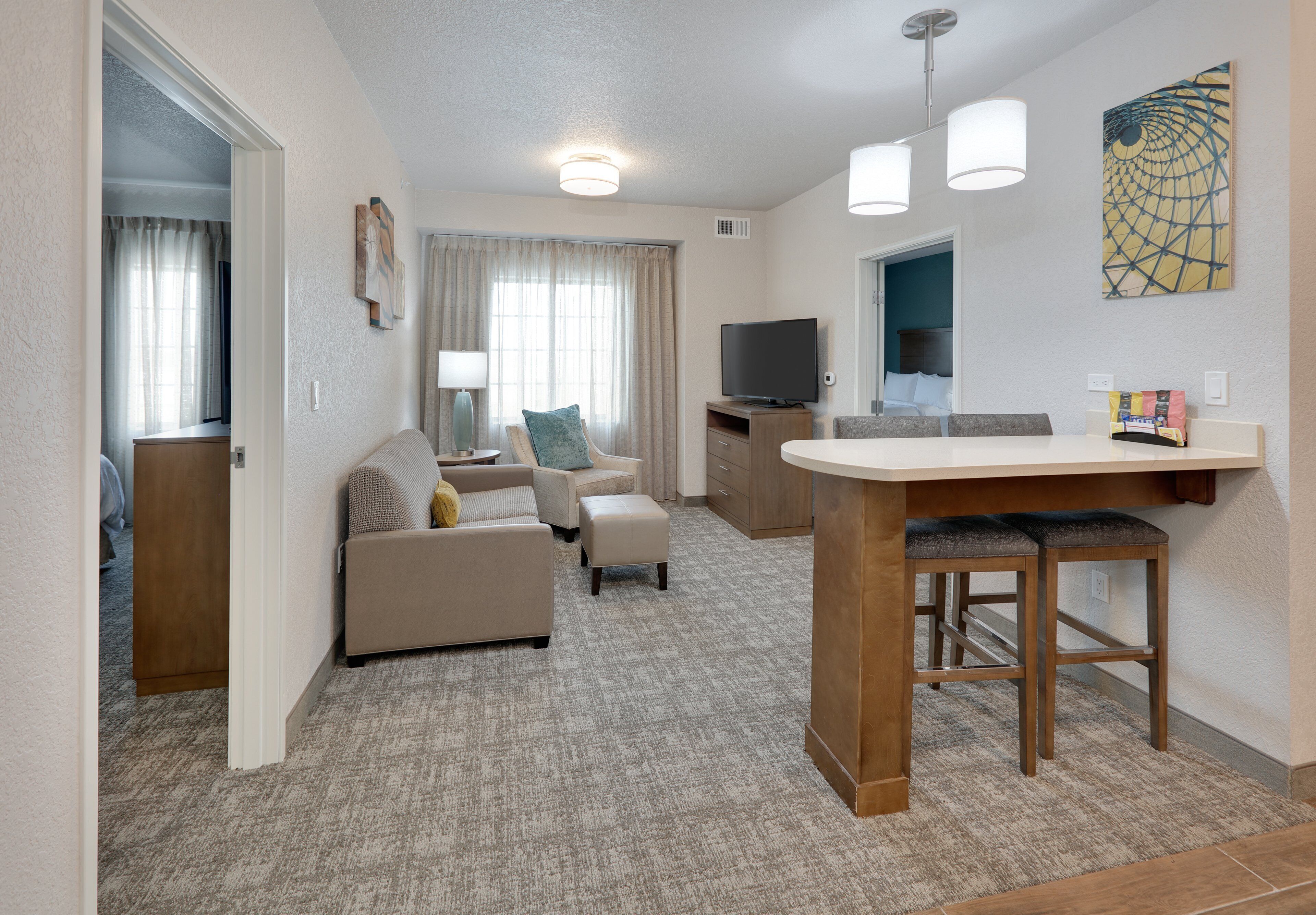 Un espace de vie compact comprenant un coin cuisine, un coin repas et un espace détente avec un canapé et un pouf.