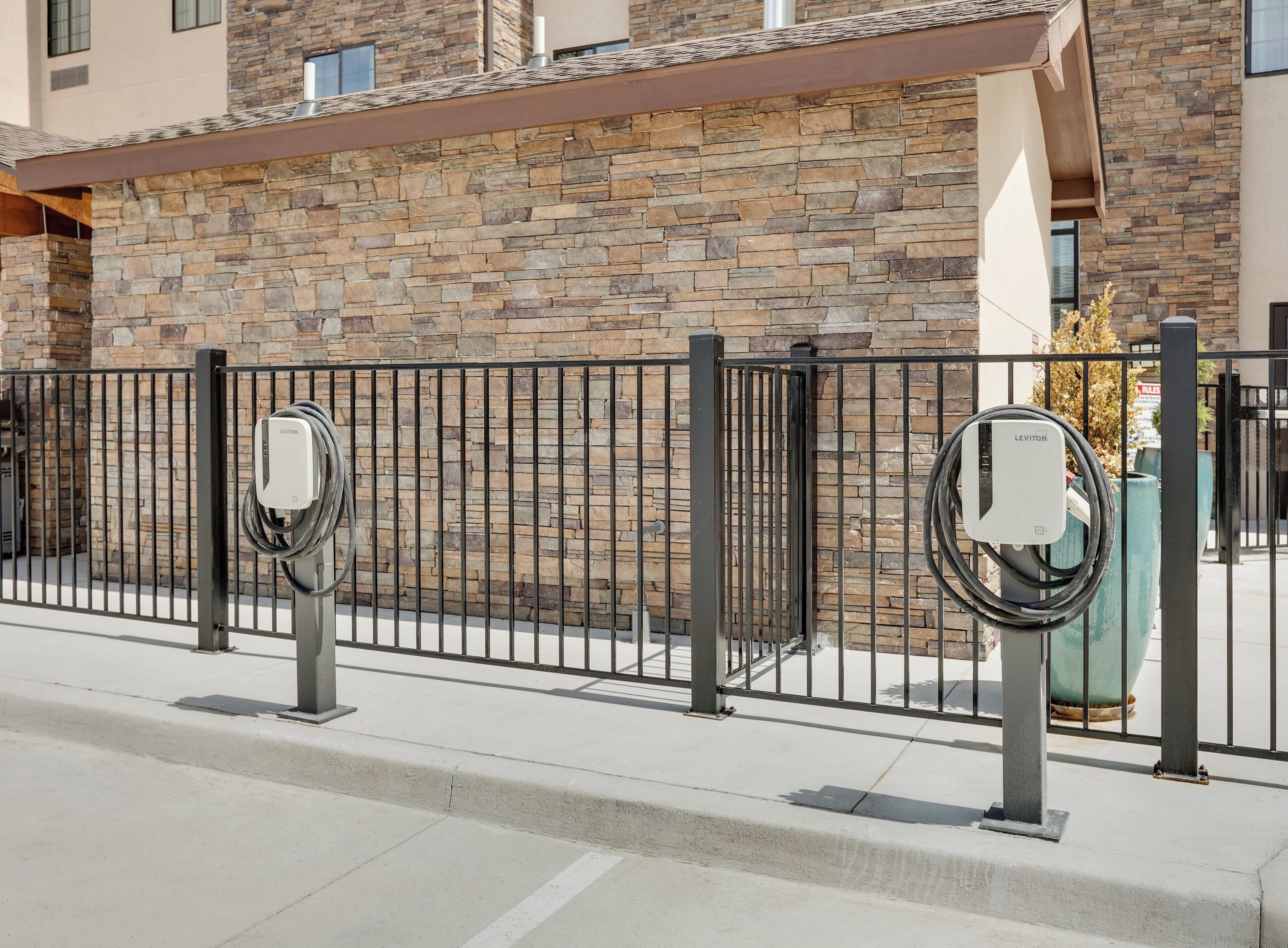 A parking area with electric vehicle charging stations, a stone wall, and a metal fence.