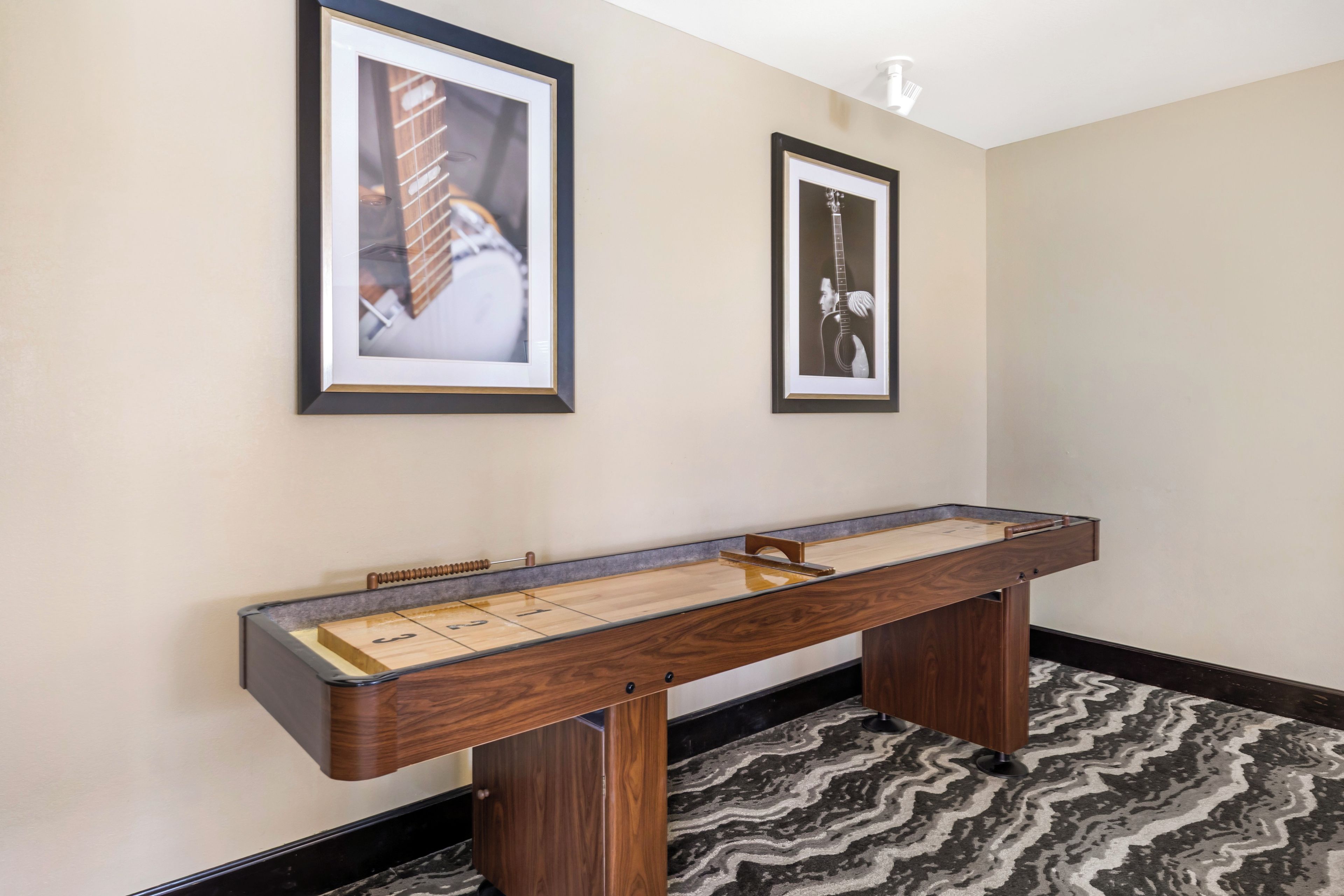 A room with a foosball table, two framed pictures on the wall, and a patterned carpet.