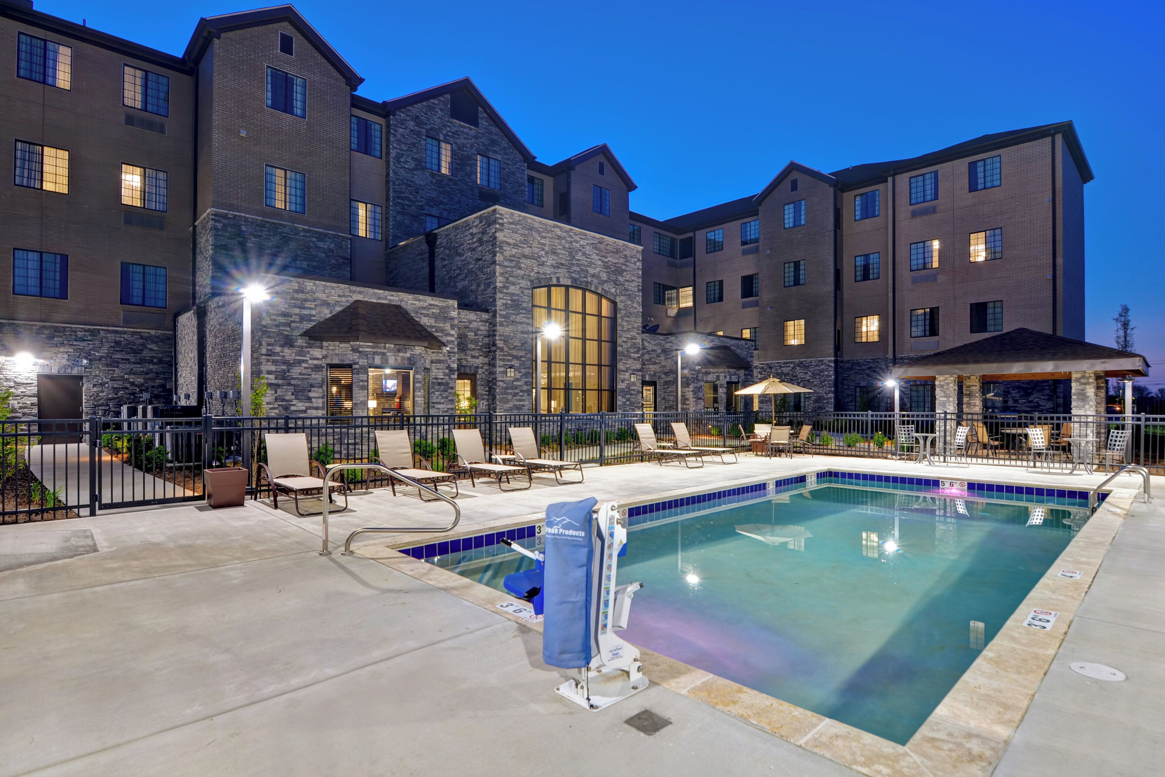 A hotel with a swimming pool, outdoor seating, and a stone facade.