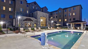 A hotel with a swimming pool, outdoor seating, and a stone facade.