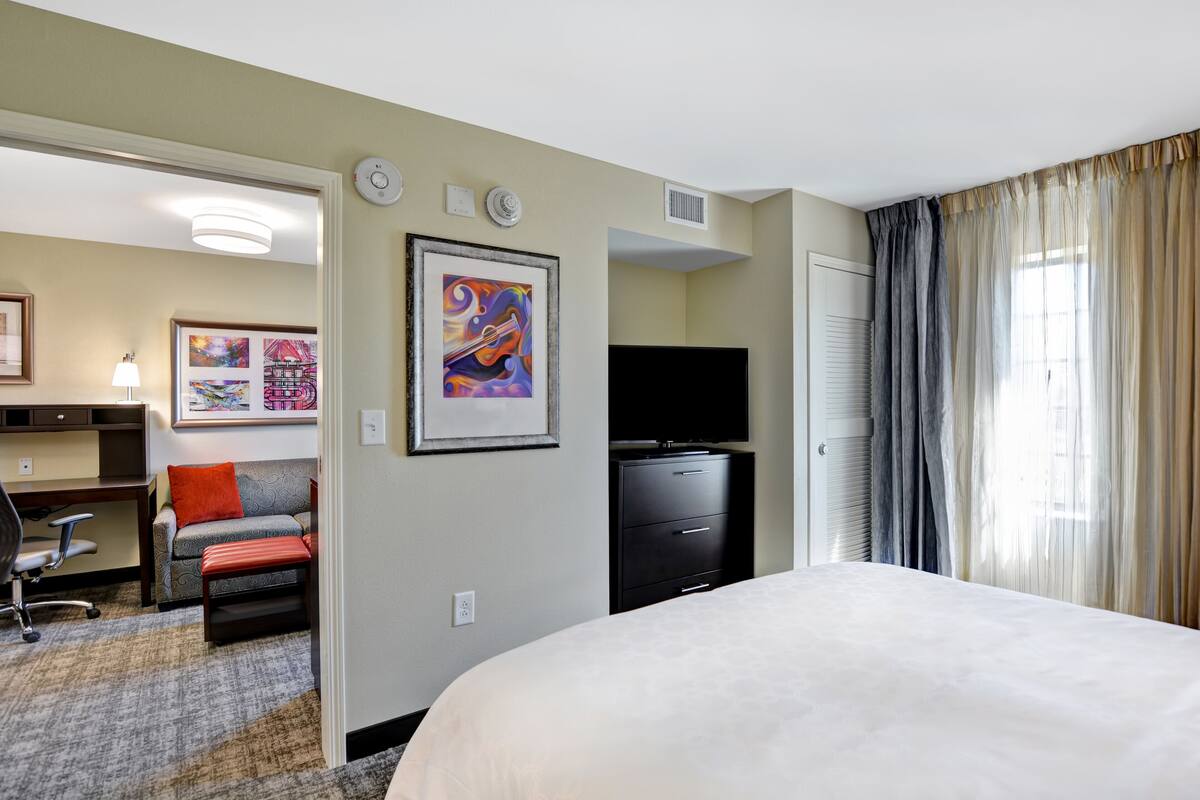 A hotel room with a large bed, a desk with a chair, a TV, and artwork on the walls.