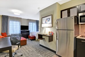 Quarto de hotel com cozinha compacta, uma cama, televisão e secretária.